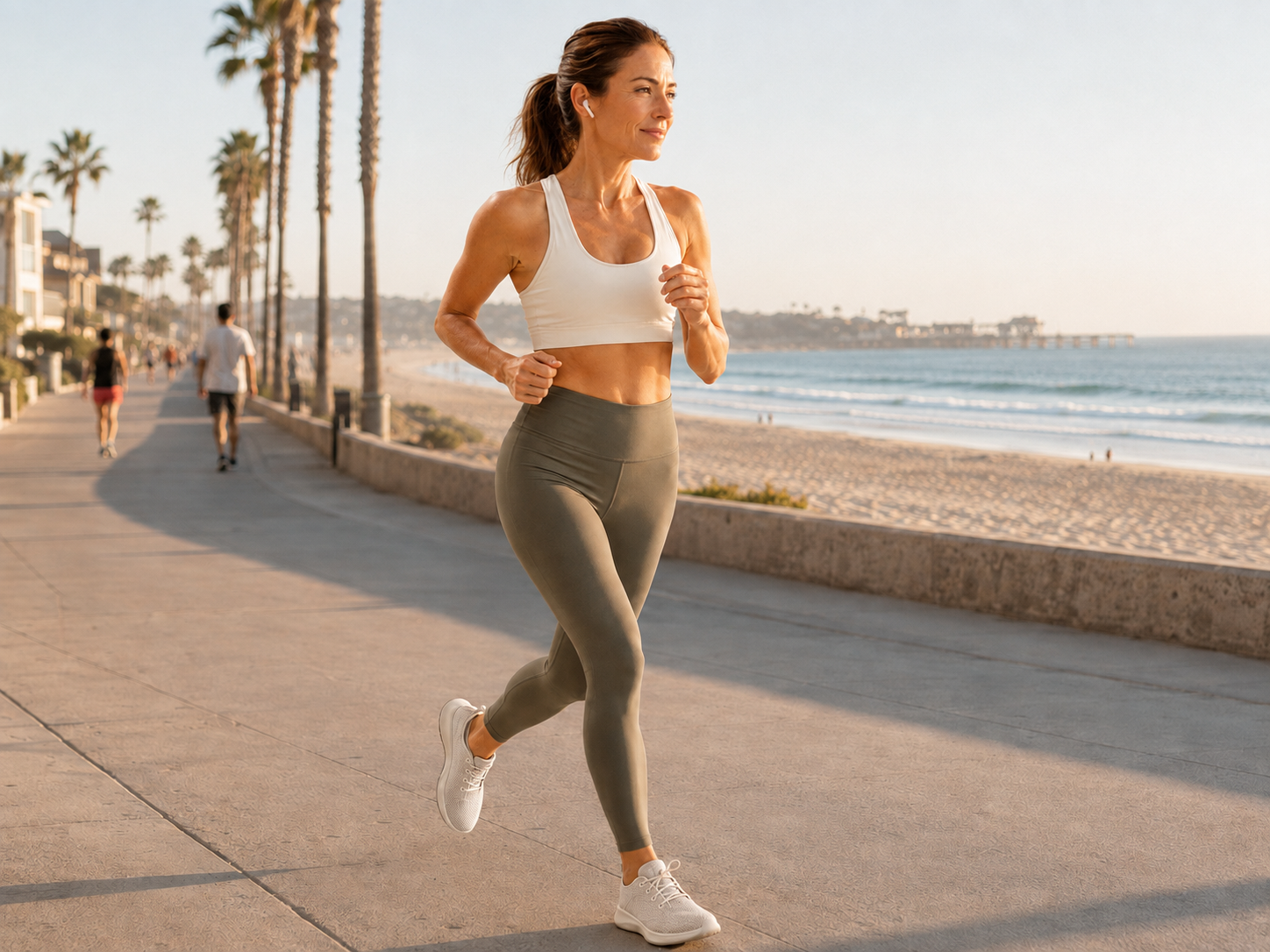 A runner on a palm-lined coastal boardwalk at golden hour, the beach and ocean stretching out beside her